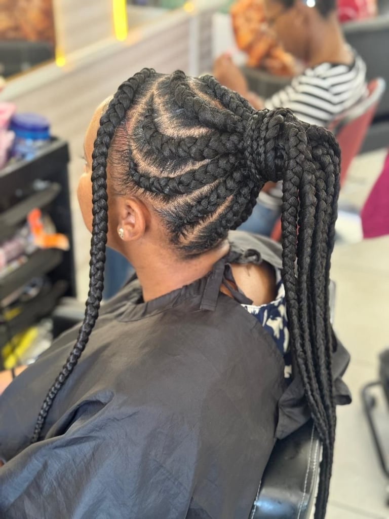 Back view of a person with long braided hair styled with decorative curved patterns, sitting in a salon chair