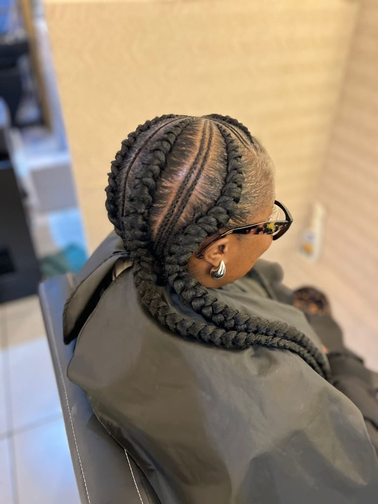 Person wearing braided hair styled in cornrows pulled back, viewed from behind, wearing olive green shirt and glasses