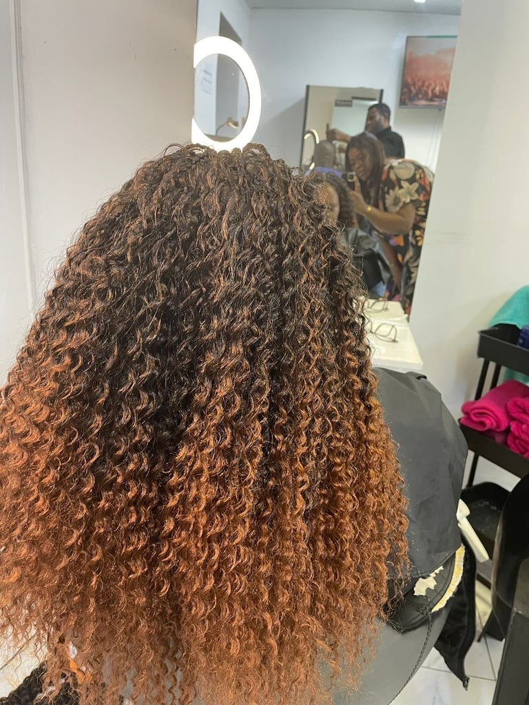 Back view of person with long, voluminous curly auburn hair in a salon mirror with ring light