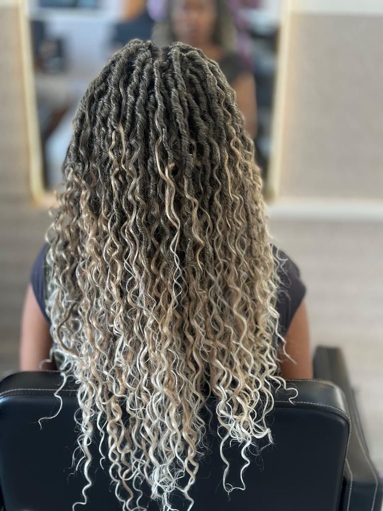 Rear view of a person with long, curly locs in shades of gray and blonde, sitting in a salon chair