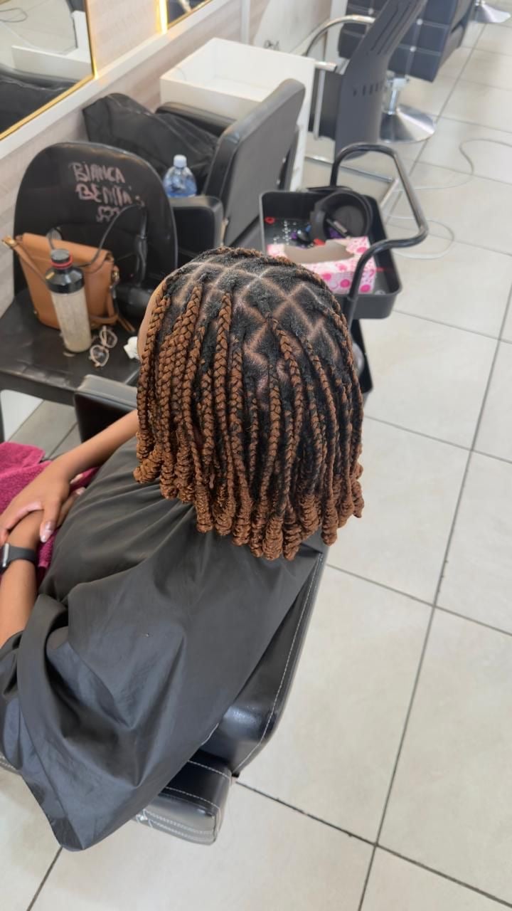 Person with brown braided hair sitting in salon chair, view from behind